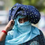 A woman uses her bag to protect herself from the sun, on a hot summer day, in New Delhi