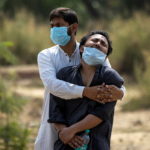 FILE PHOTO: A man is consoled by a relative before his father's burial at a graveyard in New Delhi