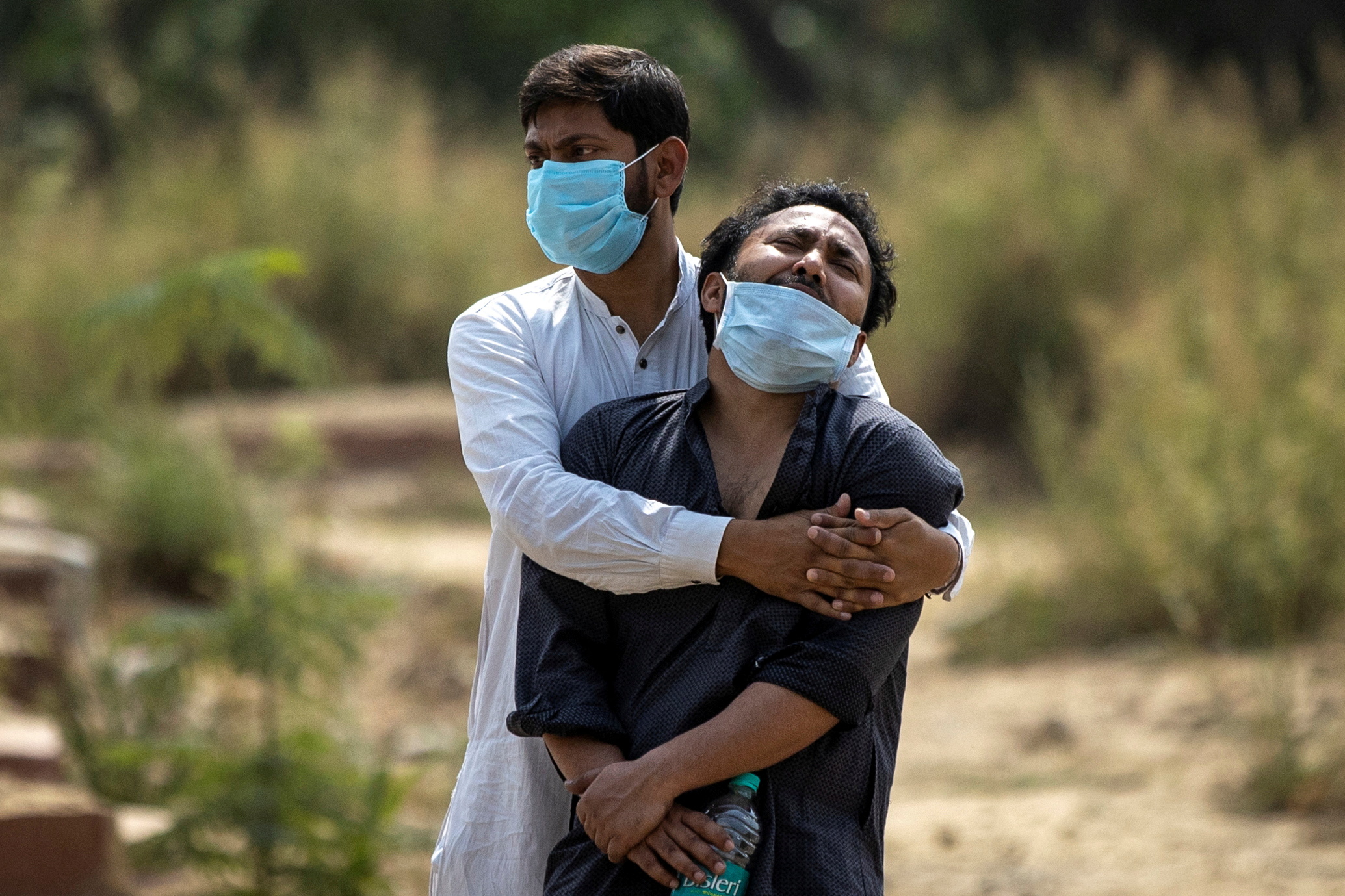 FILE PHOTO: A man is consoled by a relative before his father's burial at a graveyard in New Delhi