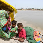 A woman and chidren sit outside their tent after taking refuge on a higher ground following rains and floods during the monsoon season in Jamshoro