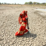 FILE PHOTO: A woman walks on the bottom of a dried pond on a hot day in Mauharia village