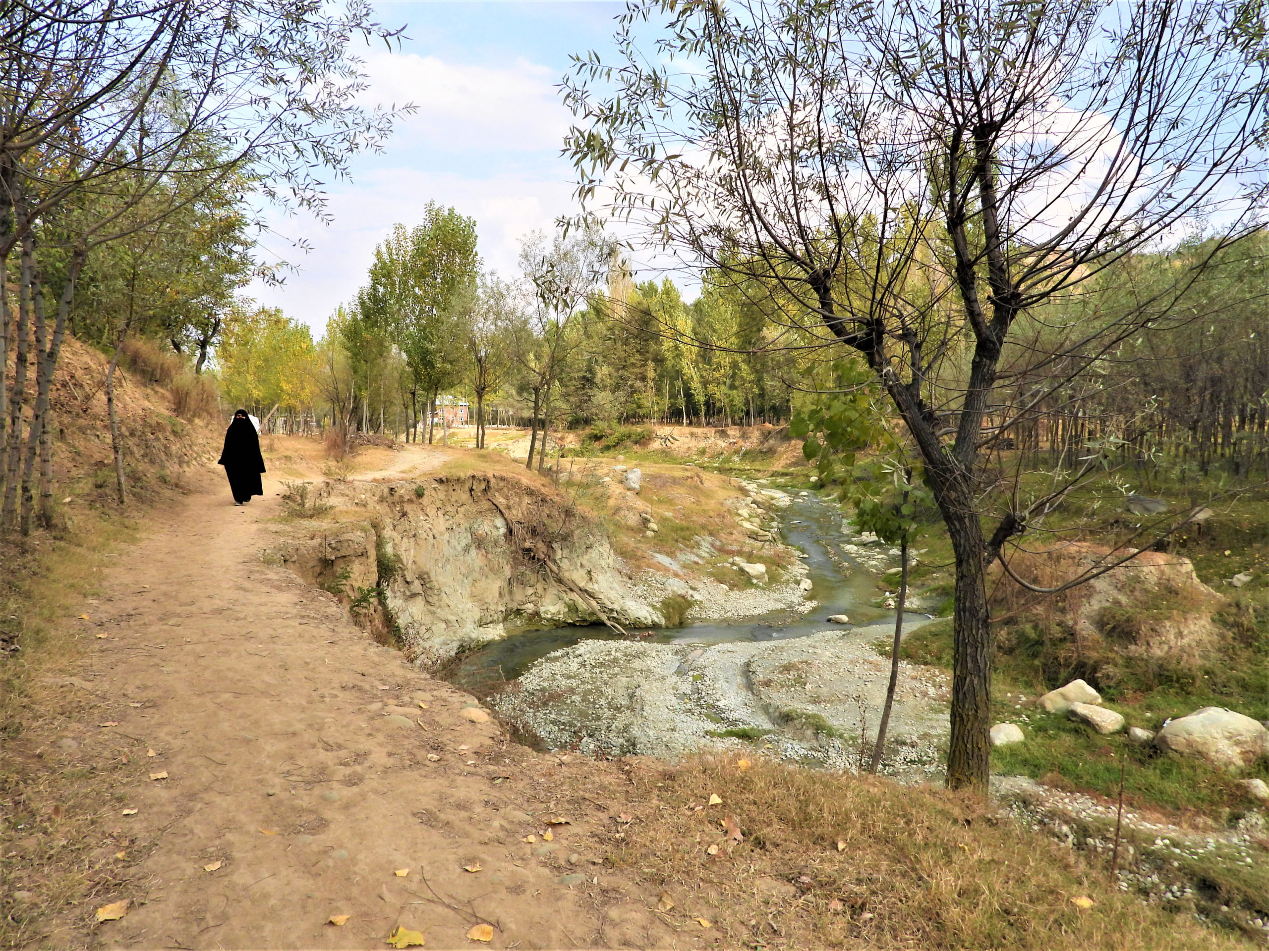 A veiled woman walks on a road damaged by flooding exacerbated by glacial melt, in Kashmir's Chendargund village, India, October 12, 2022. Thomson Reuters Foundation/Athar Parvaiz